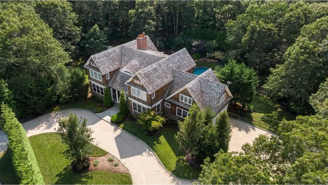 A large house surrounded by trees, with a curved driveway in front.
