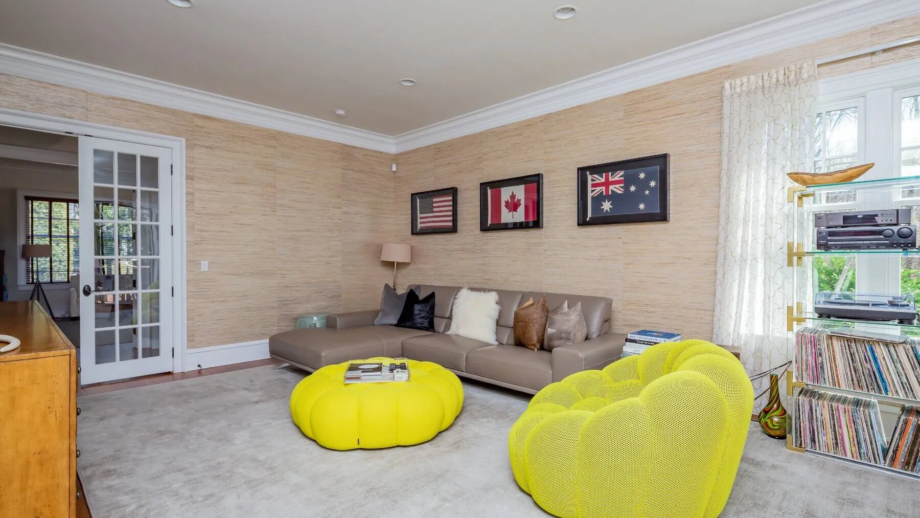 A living room with a sectional sofa, bright yellow seating, and framed flags on the wall.