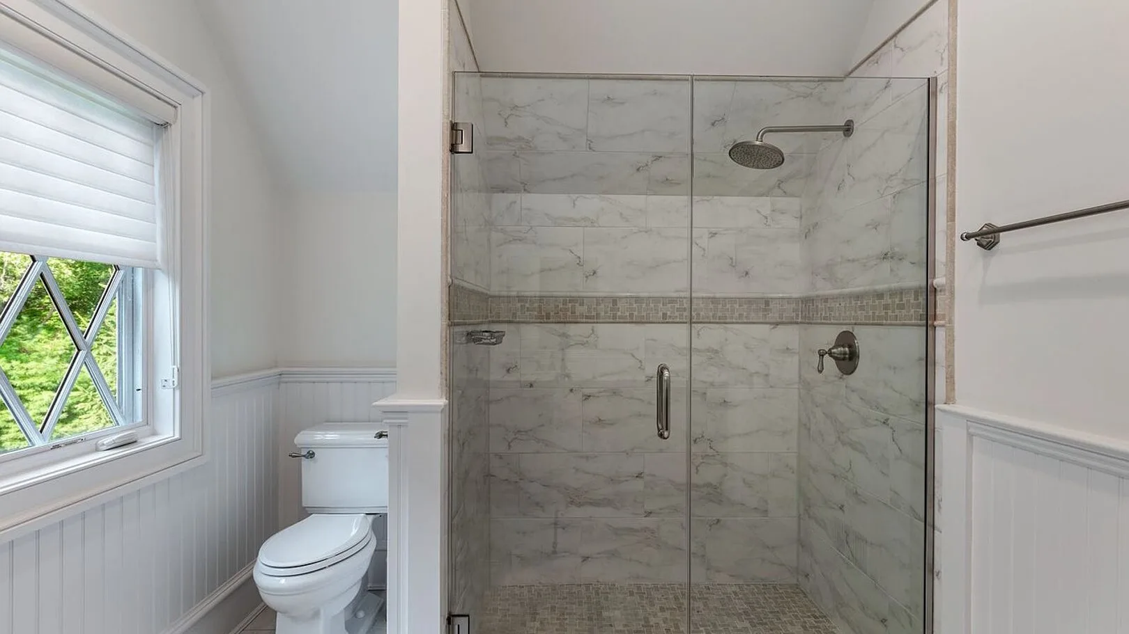 A bathroom with a glass-enclosed shower and a window.