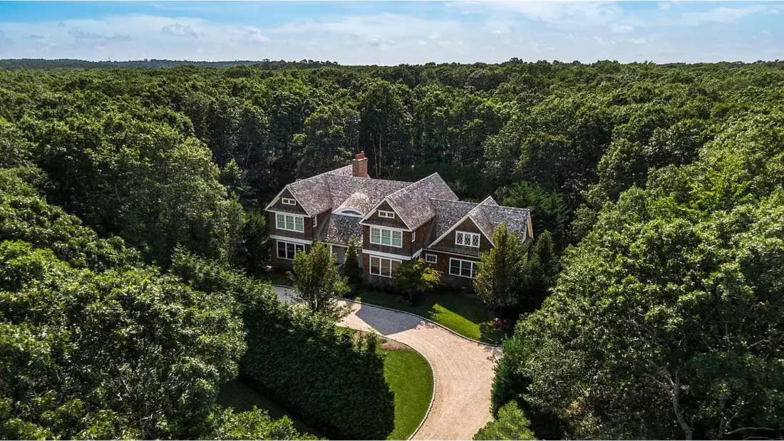 A large house sits among dense green trees beside a curved driveway.