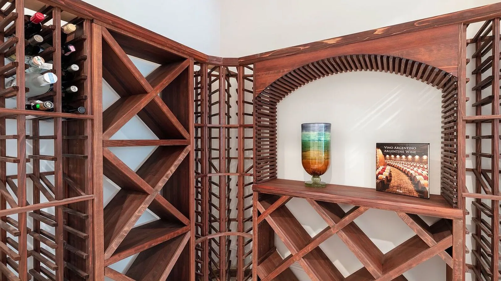 A wooden wine-storage display with bottle racks and a decorative arched shelf.