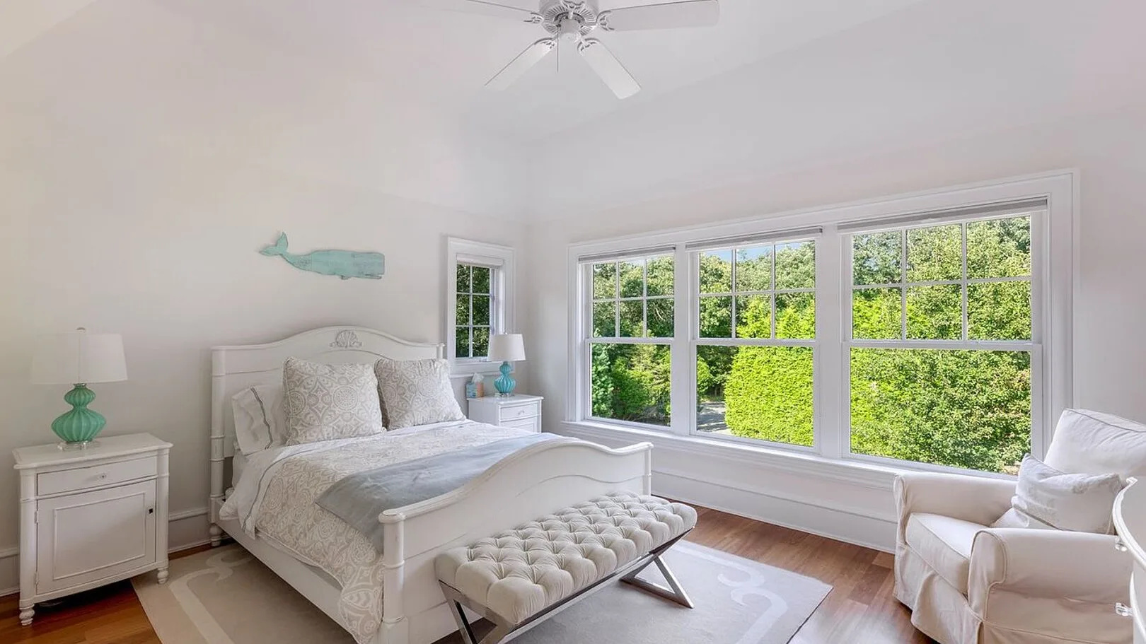 A bright bedroom with a neatly made bed beside large windows overlooking greenery.