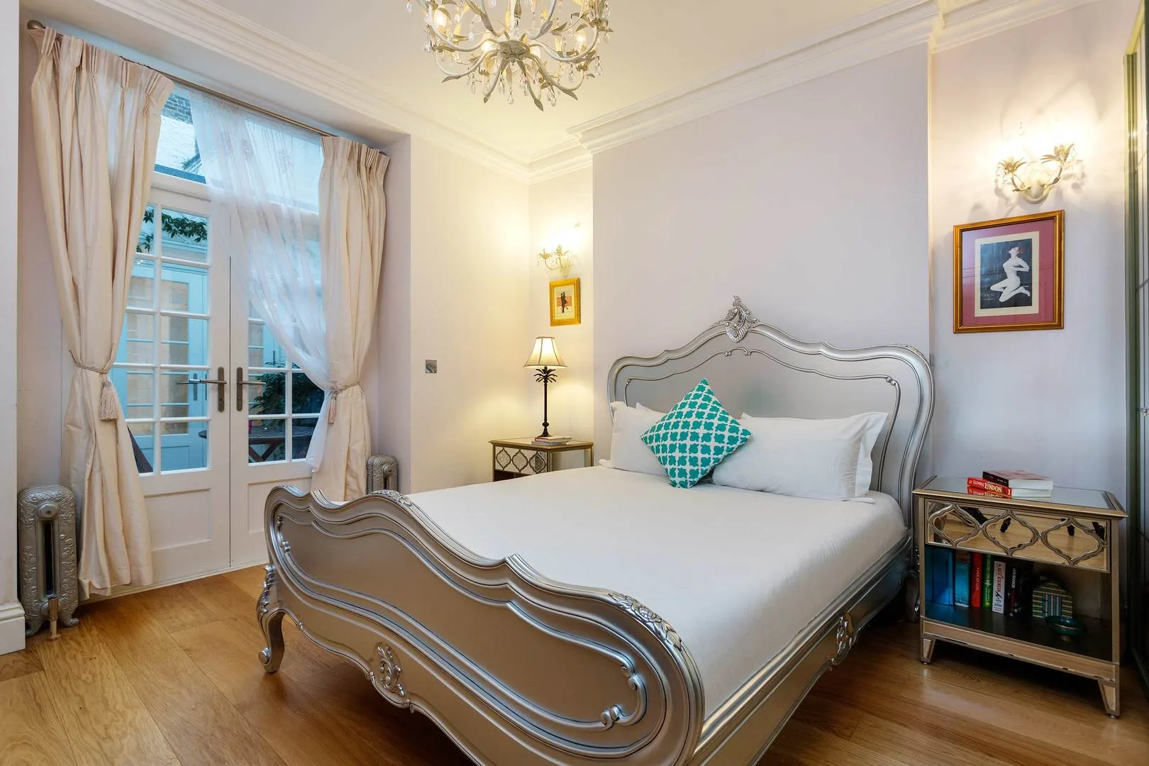 A bedroom with a carved bed, bedside tables, and tall curtained windows.