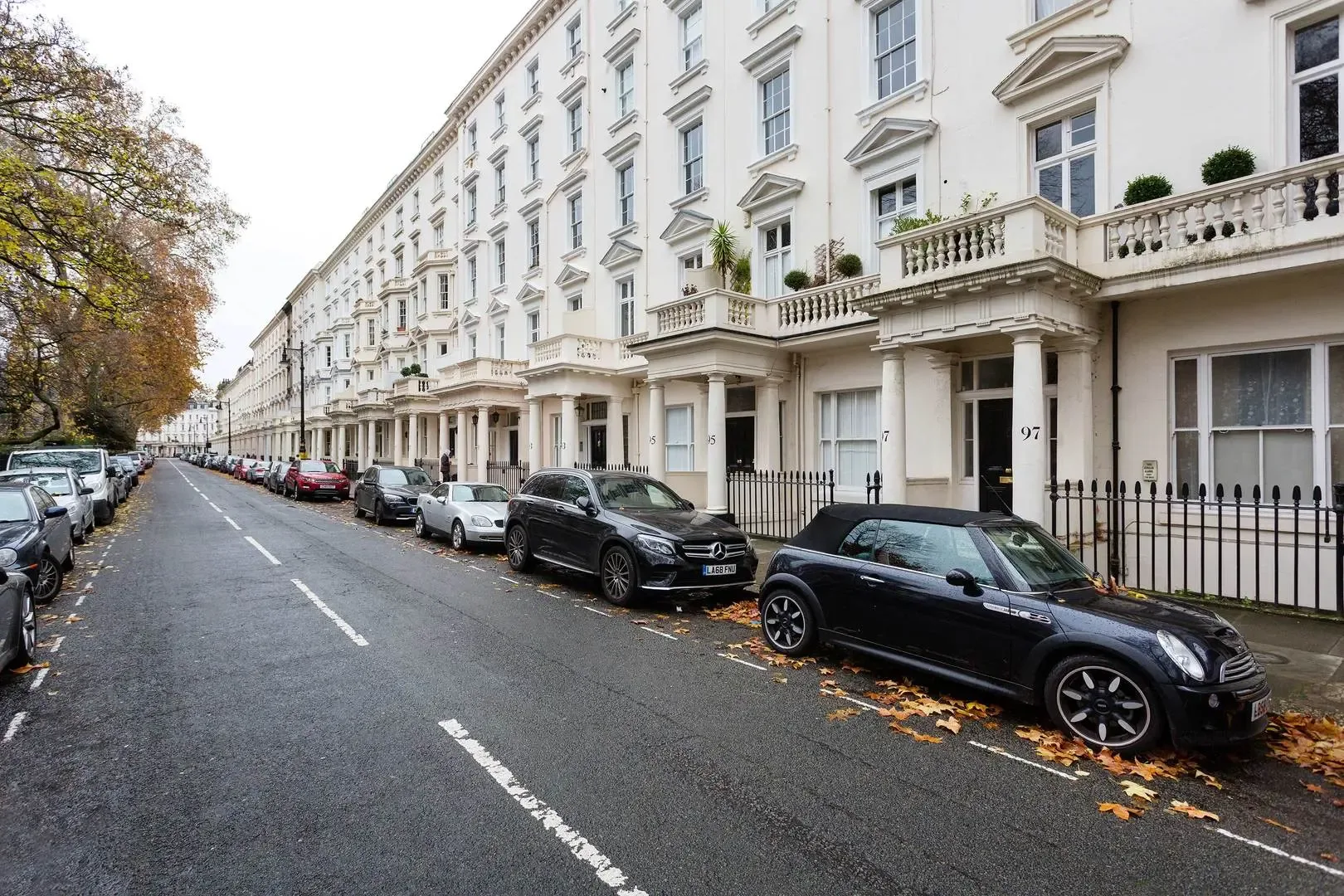 A row of white townhouses lines a street with parked cars.