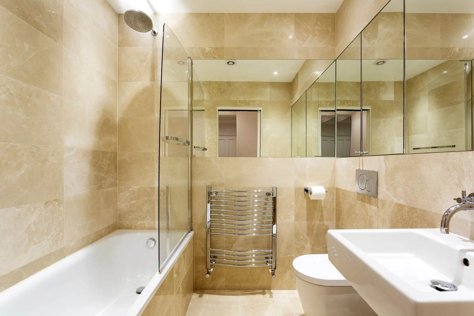 A bright bathroom with a bathtub, glass shower screen, sink, and wall mirror.