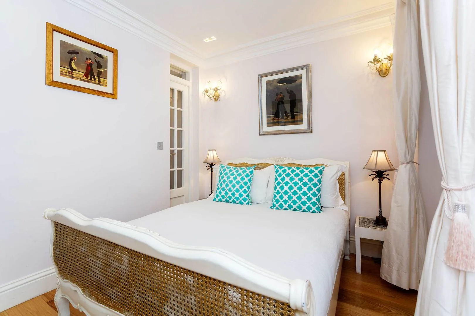 A bright bedroom with a large bed, turquoise cushions, and framed artwork.