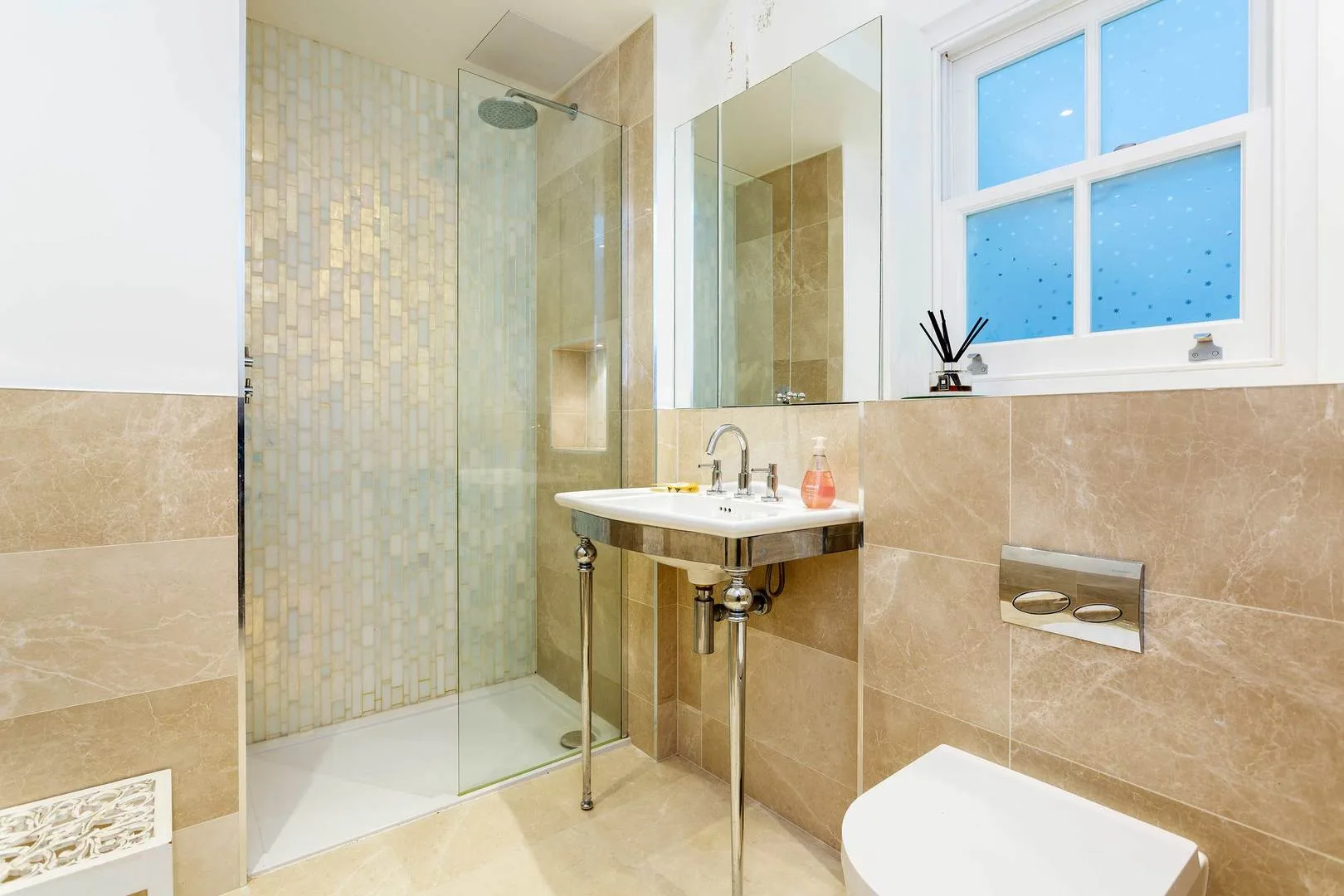 A bright bathroom with a glass shower, wall-mounted sink, and window.