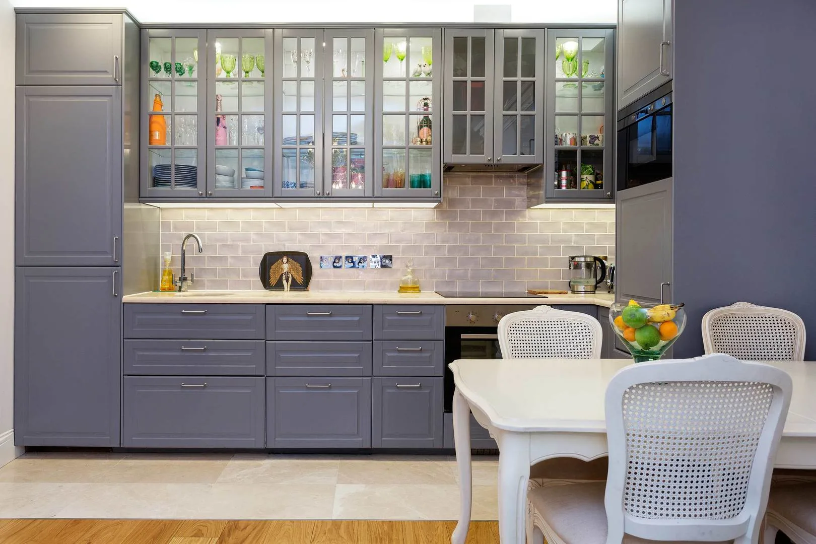 A modern kitchen with gray cabinets, a tiled backsplash, and a white dining table.