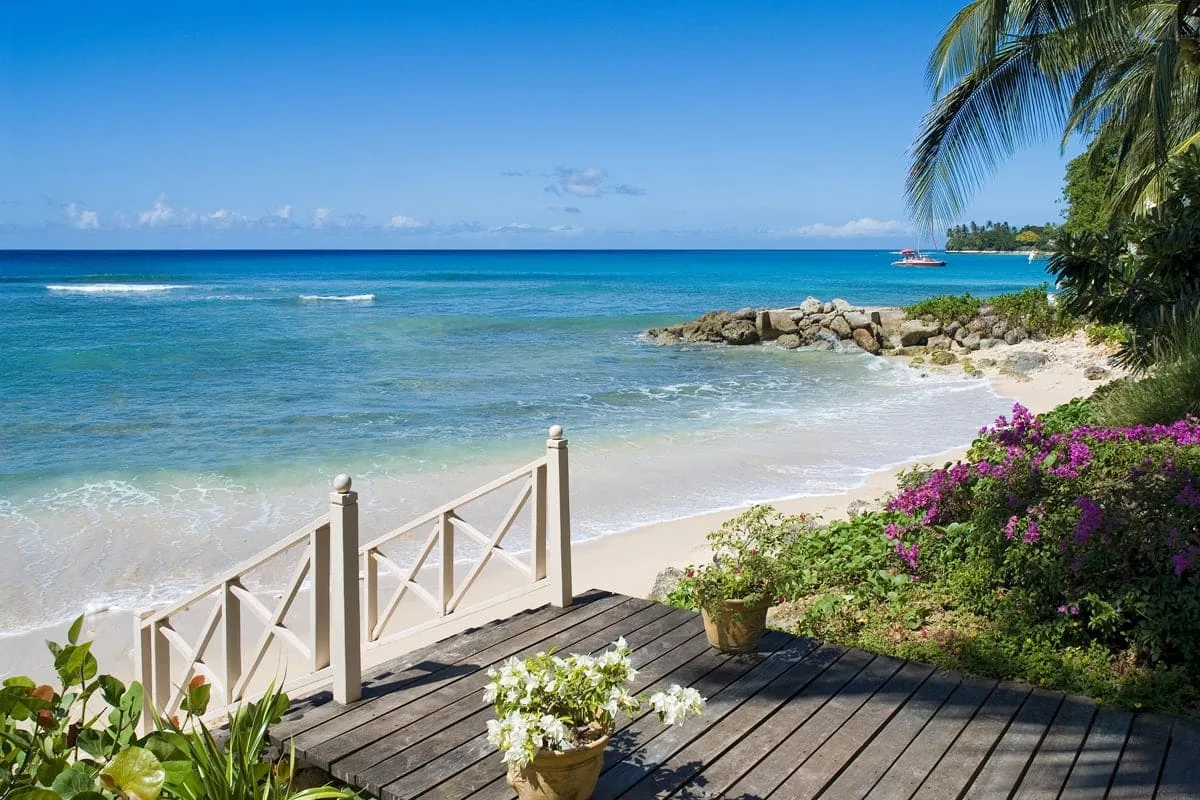 A wooden seaside deck overlooks a sandy beach and clear turquoise water.