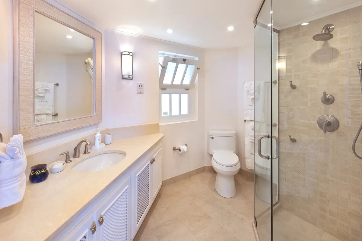 A bright bathroom with a long vanity, toilet, and glass-enclosed shower.