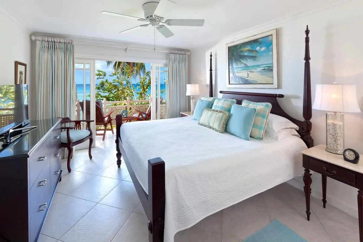 A bright bedroom with a large bed and sliding glass doors opening to a balcony.