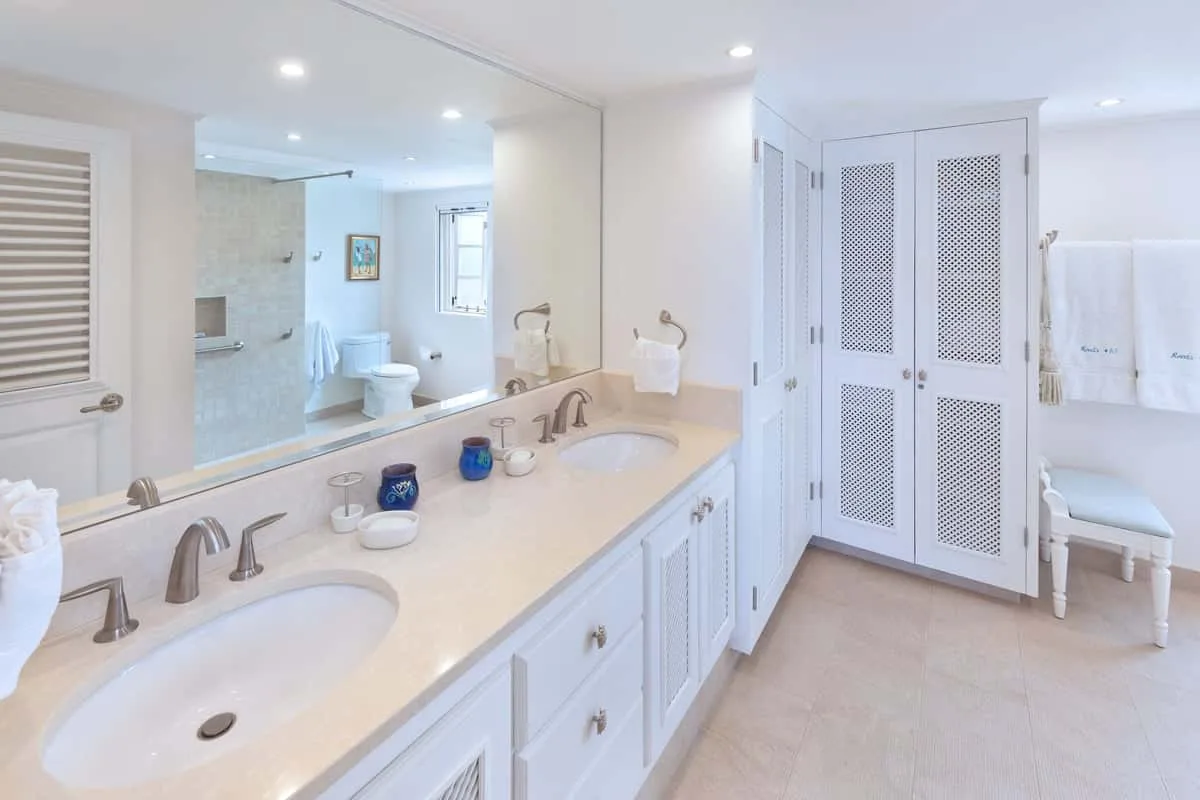 A bright bathroom with a long double vanity and a shower area.