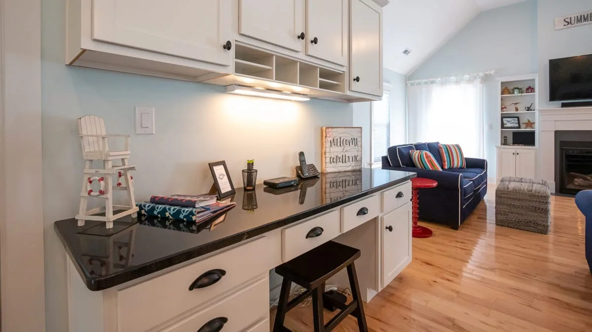 A bright living room with a dark sofa, television, and long kitchen counter.