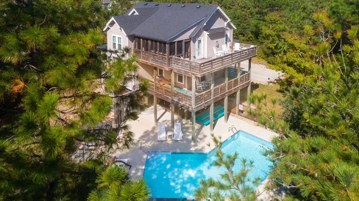 Una casa elevada con terrazas envolventes da a una piscina entre árboles.