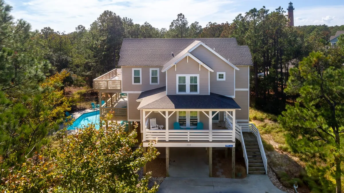 A raised house with a covered porch sits among trees beside a swimming pool.