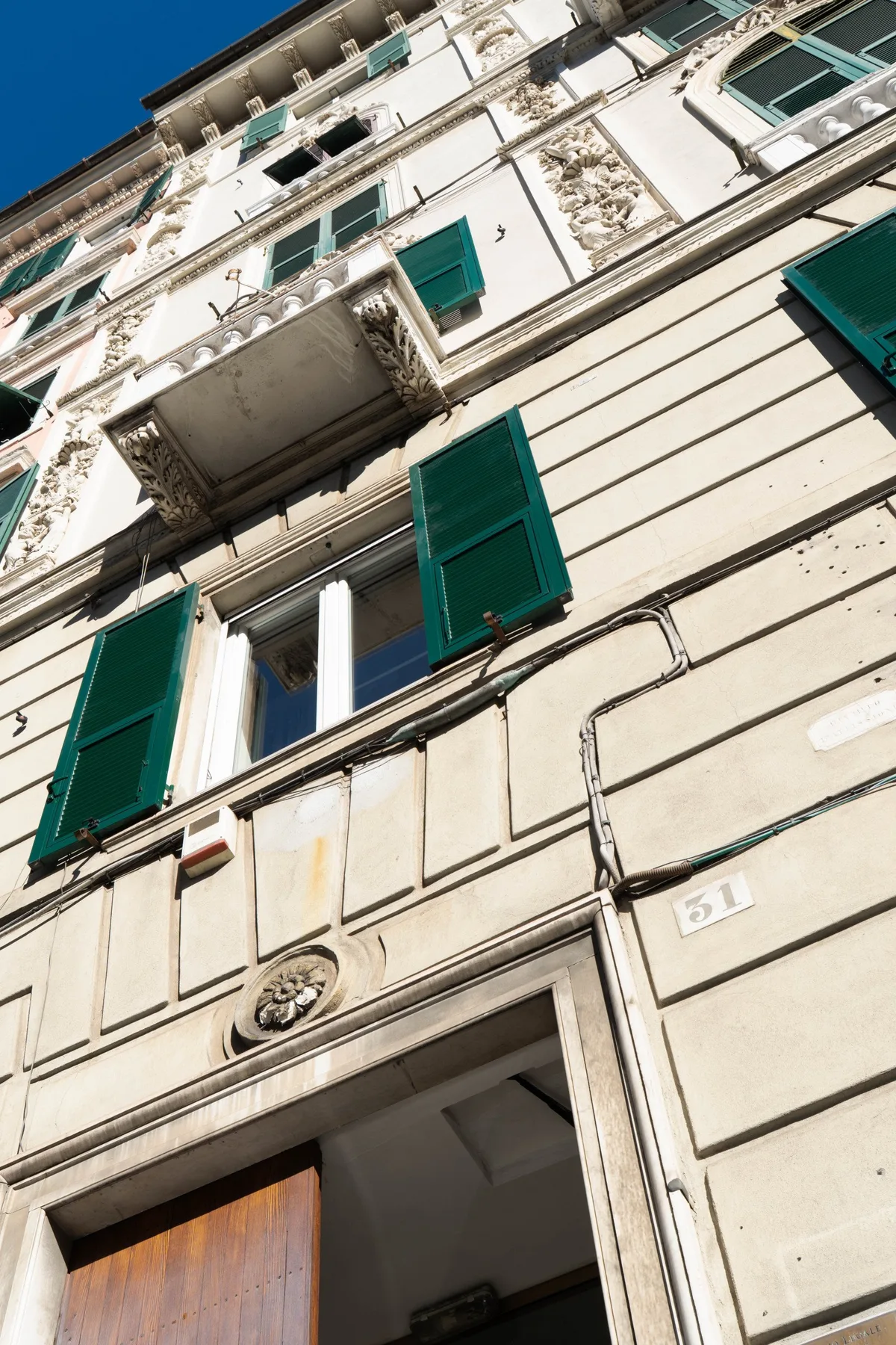 A sunlit building facade with green shutters and an open doorway.