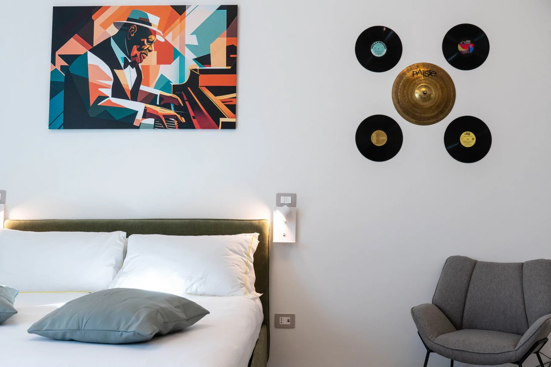 A bedroom with a bed beneath colorful wall art and a grouping of records.