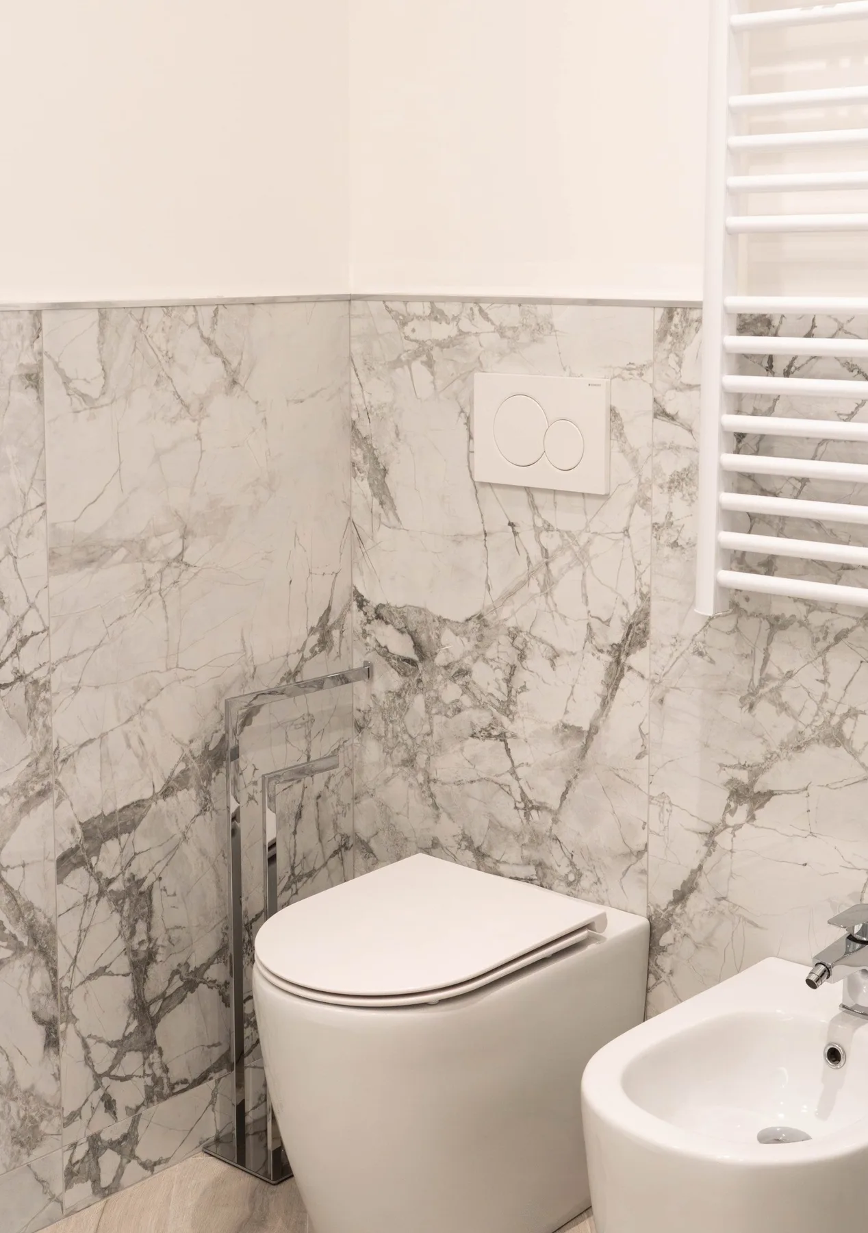 A bathroom with a wall-mounted flush plate, toilet, and sink.