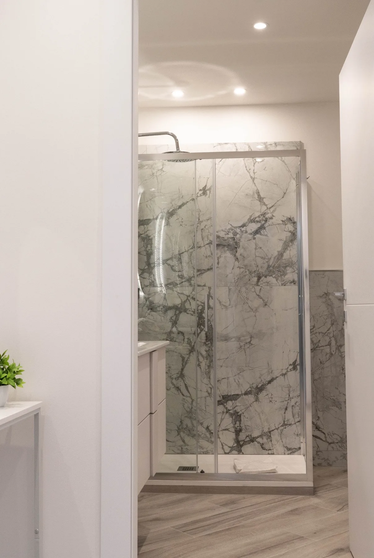 A bathroom with a glass shower and marble-patterned walls.