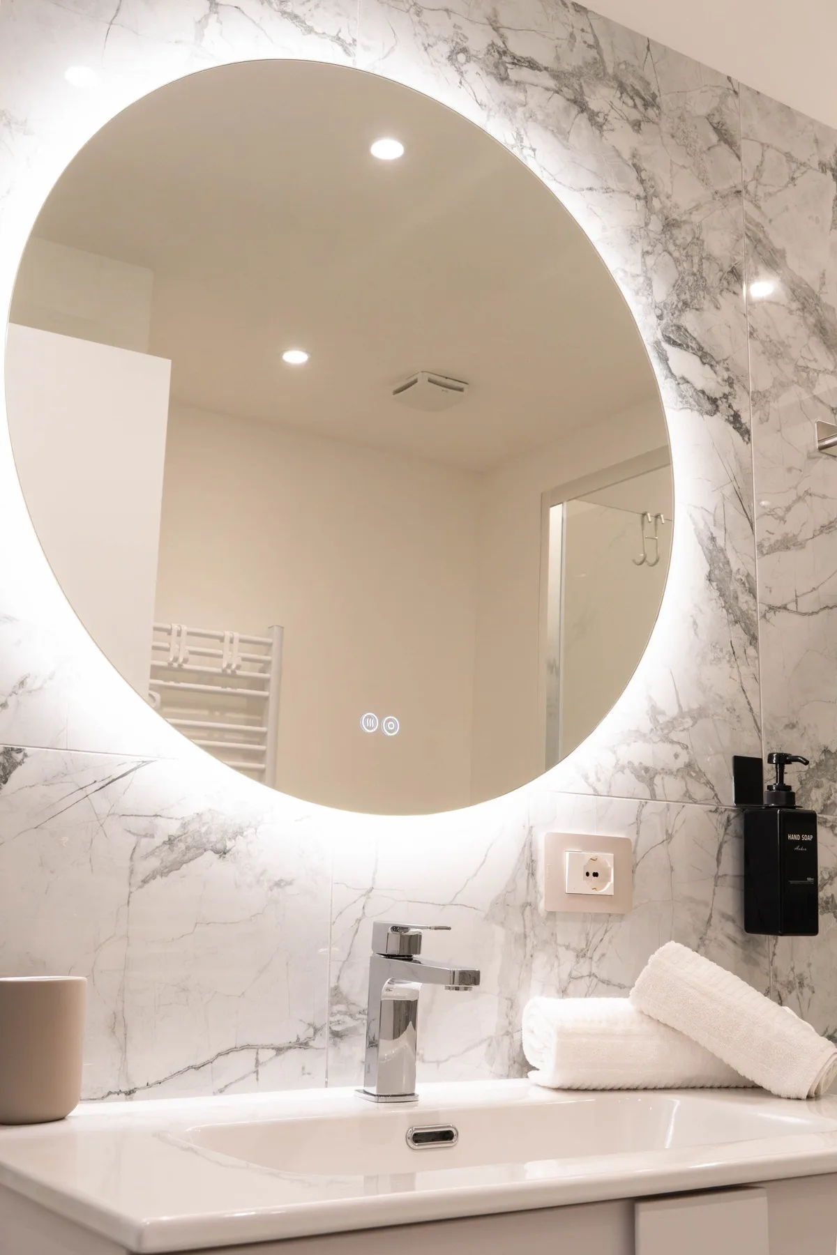 A bathroom vanity with a large illuminated round mirror above the sink.