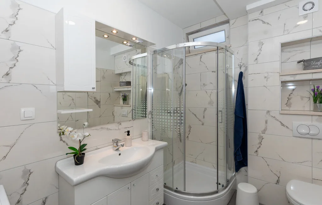 Un baño con azulejos, una ducha de vidrio curvada y un lavabo.
