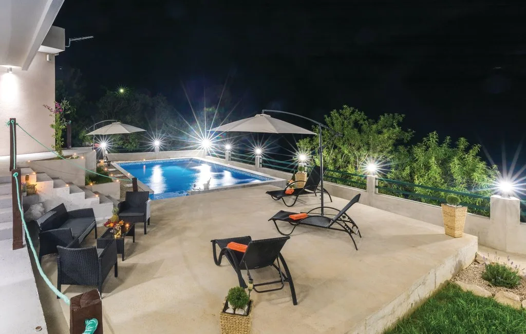 Un patio nocturno con asientos da a una piscina iluminada.