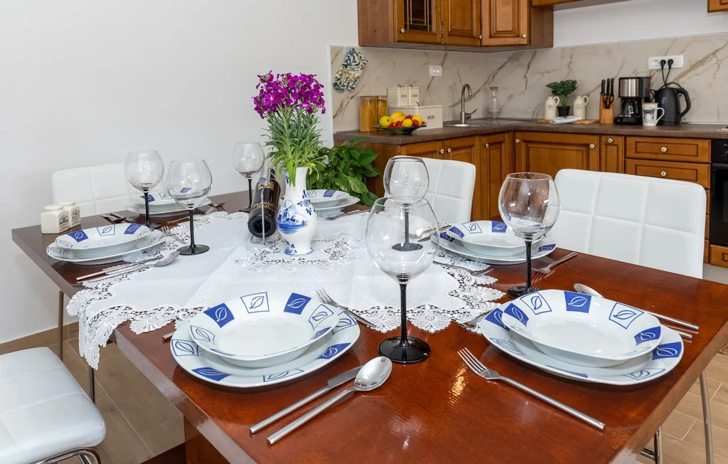 Una mesa de comedor puesta con platos y vasos está junto a una cocina.