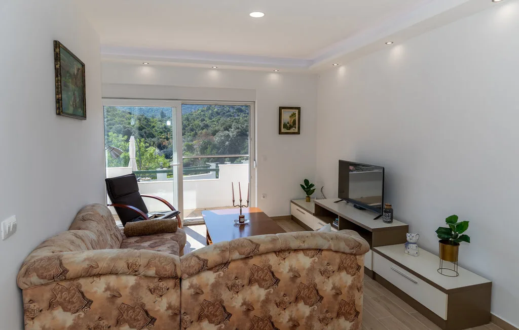 Una sala de estar con asientos, un televisor y puertas corredizas de vidrio que dan a un balcón.