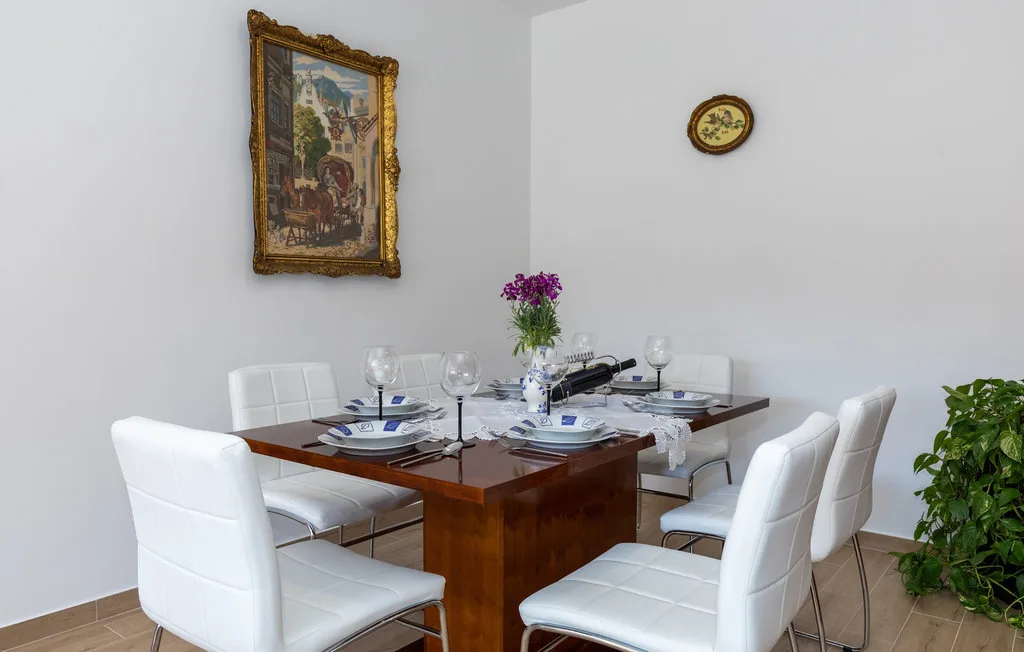 Comedor con una mesa de madera puesta con vajilla y asientos blancos.