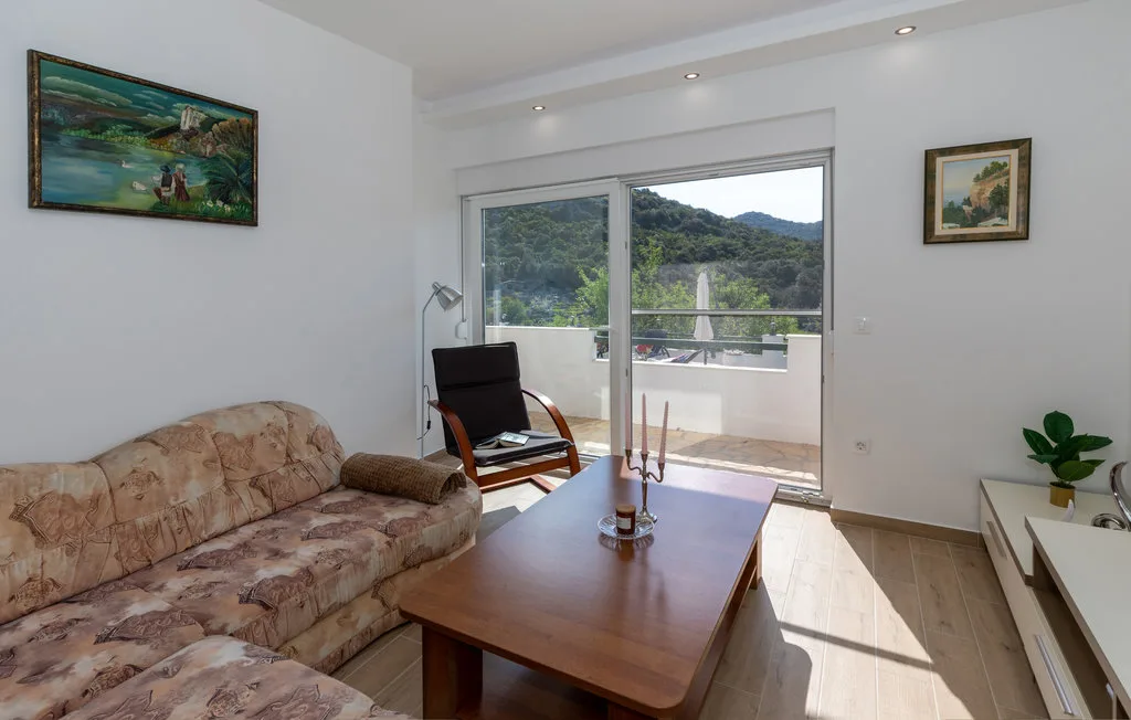 Una sala de estar con asientos, una mesa de centro y puertas corredizas de vidrio hacia un balcón.