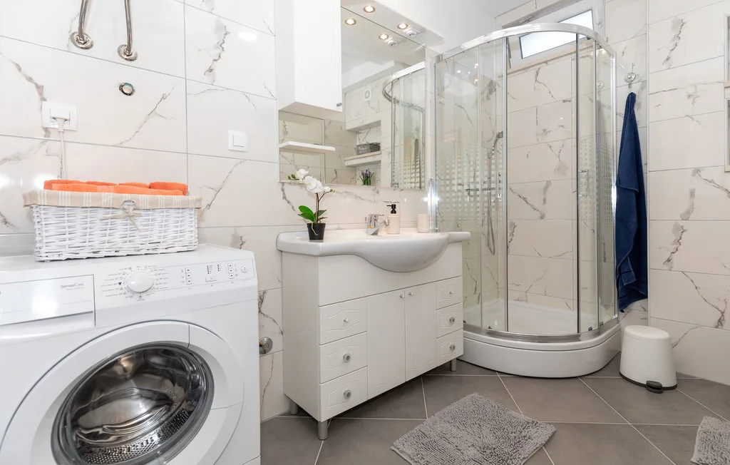 Un baño luminoso con azulejos, lavabo, ducha y lavadora.