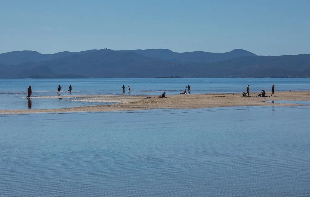 Una playa amplia y aguas poco profundas se extienden hacia montañas lejanas.
