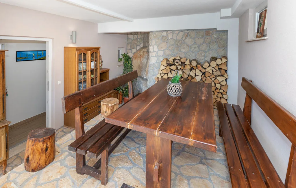 Un comedor rústico con una mesa larga de madera y leña apilada junto a una pared de piedra.