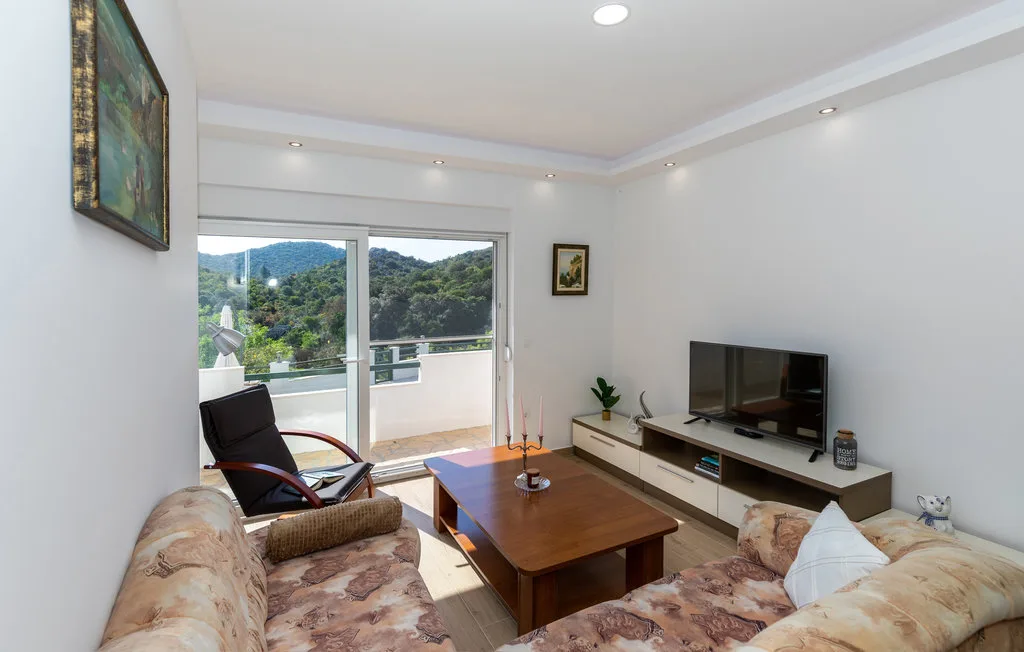 Sala de estar con asientos, un televisor y puertas corredizas de vidrio que dan a un balcón.