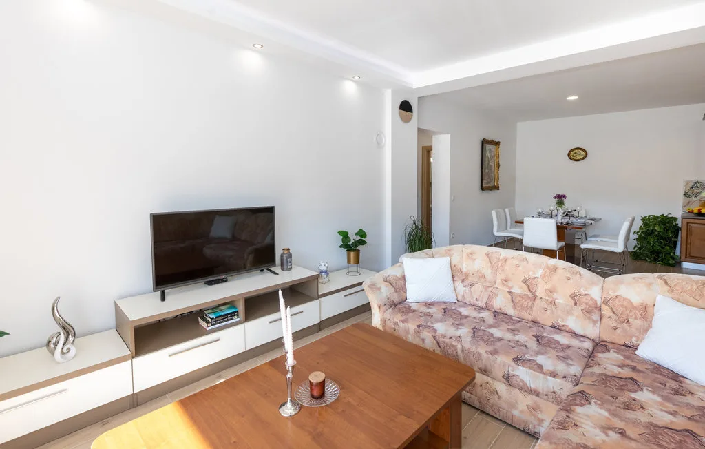 Una sala de estar con asientos, un televisor y un comedor al fondo.