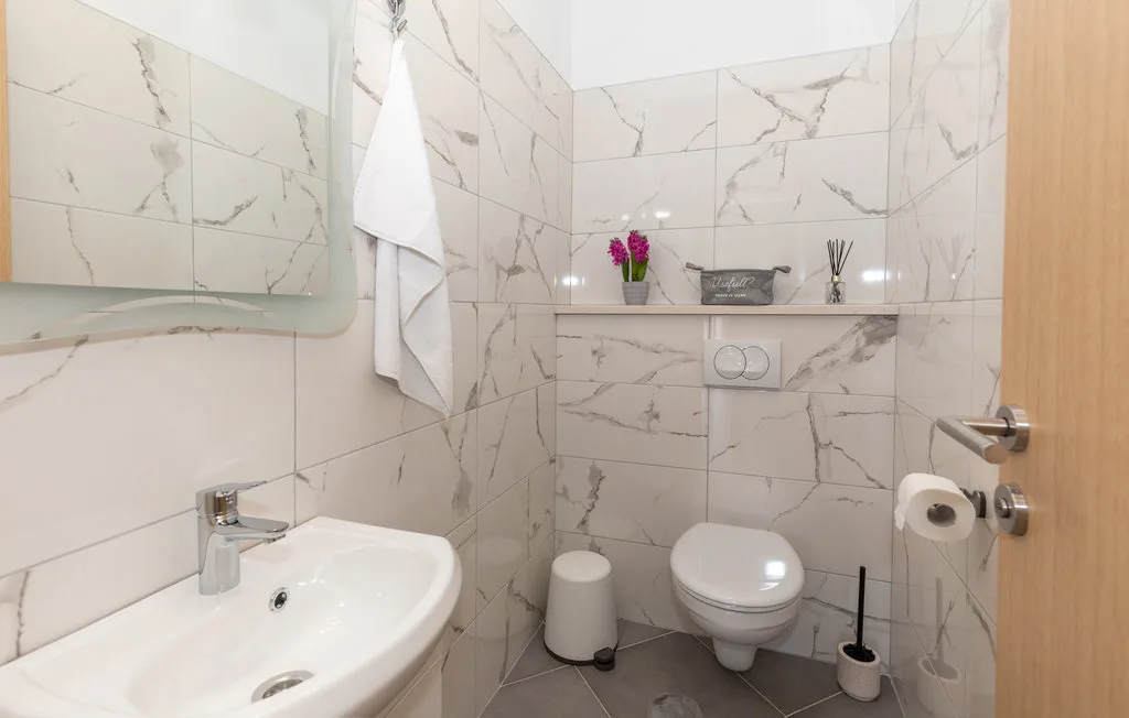 Un baño alicatado con lavabo, inodoro suspendido y una toalla doblada.