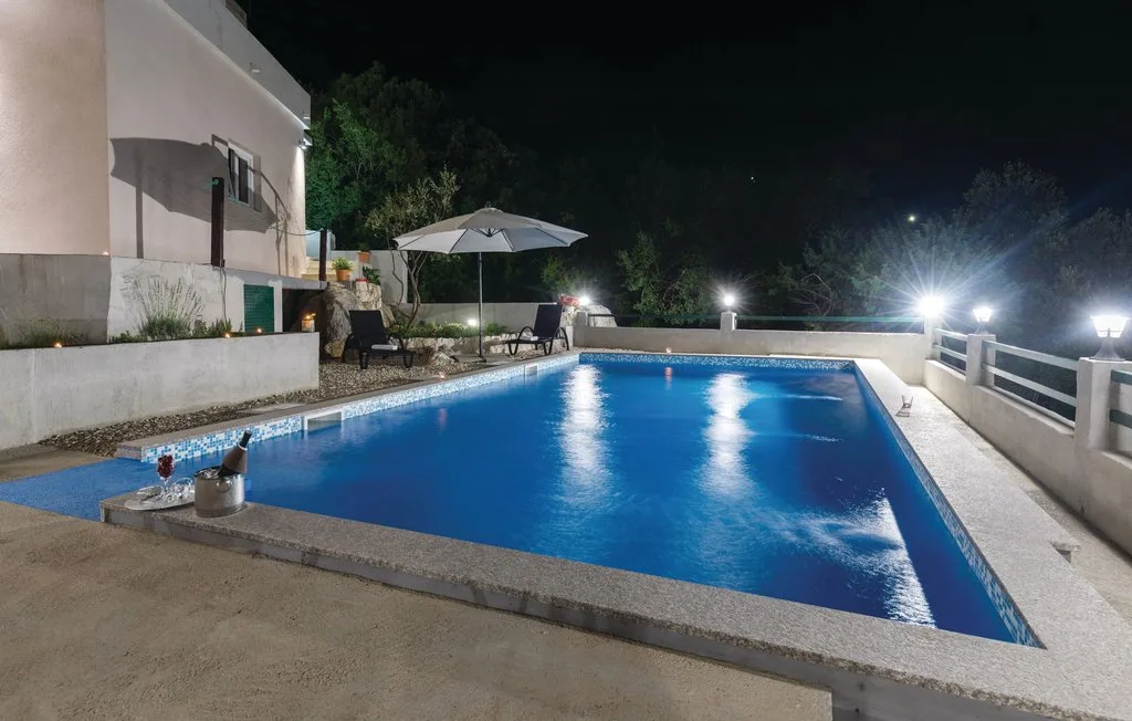 Una piscina al aire libre de noche, junto a un edificio y asientos de patio.