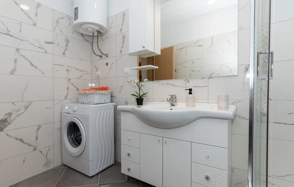 Un baño con azulejos, un lavabo con mueble y una lavadora.