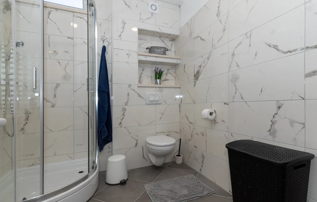 Baño alicatado con ducha, inodoro y cesto oscuro para la ropa.