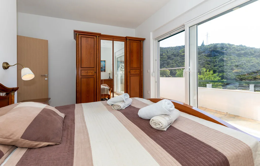 Un dormitorio con la cama tendida junto a una gran ventana con vistas a colinas verdes.