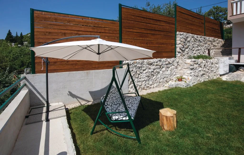 Un patio exterior con césped tiene un columpio a la sombra junto a un muro de piedra.