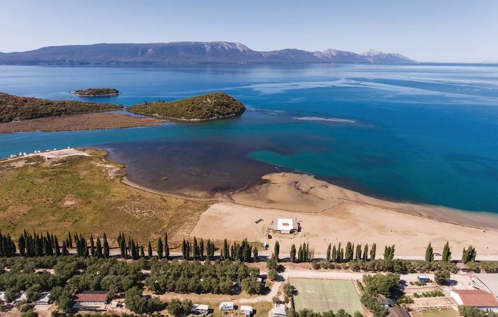 Vista aérea de un paisaje costero con una playa de arena, aguas turquesas e islotes.