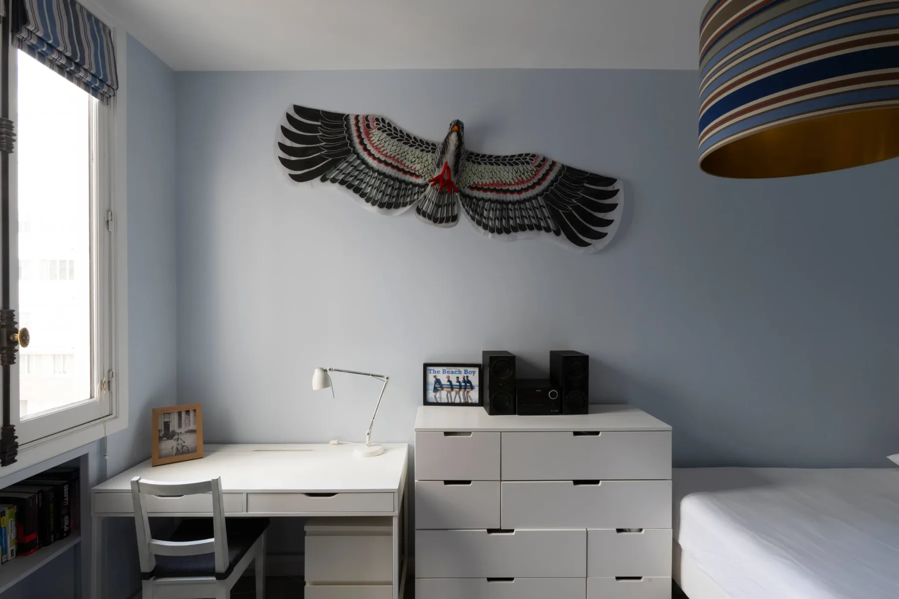 A bedroom with a desk, white drawers, and a bed.