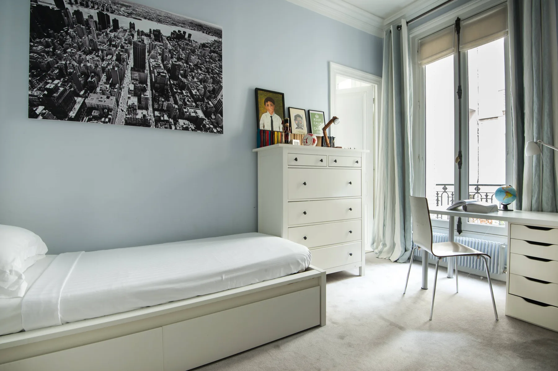 A bright bedroom with a single bed, a chest of drawers, and a desk by the window.