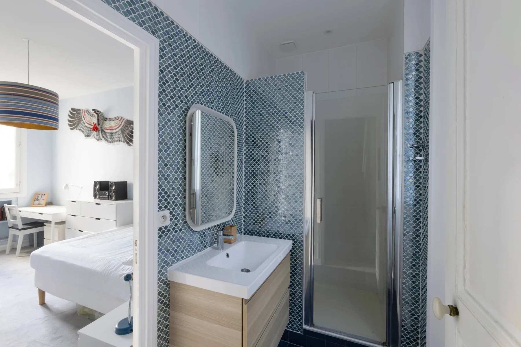 A bathroom with blue patterned tile and a sink beside the shower.