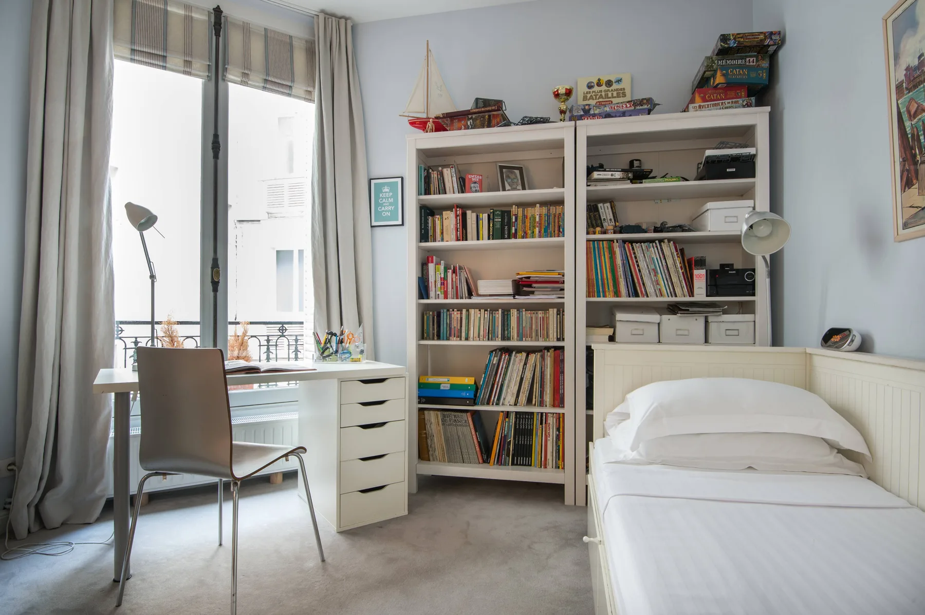 A bedroom with a single bed beside a desk and built-in bookshelves.