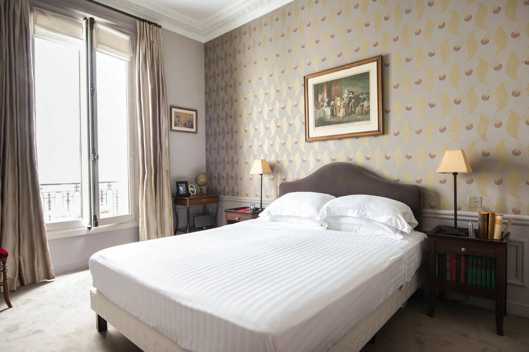 A bedroom with a neatly made bed and patterned wallpaper.