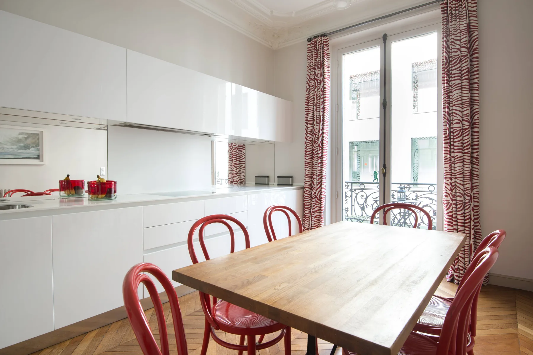 A dining area with a wooden table, red seating, and tall windows.