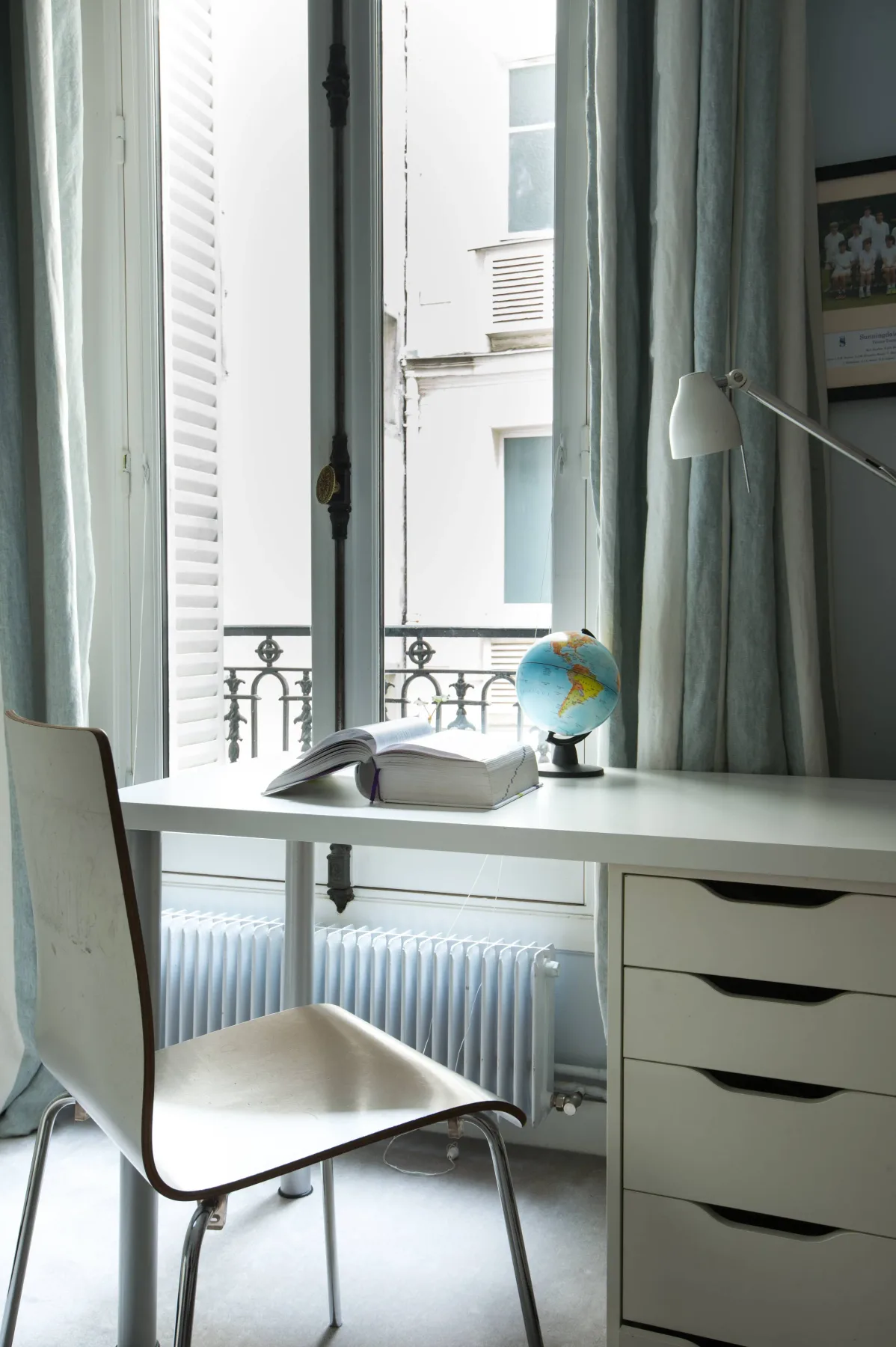 A bright desk sits beside a tall window with pale curtains.