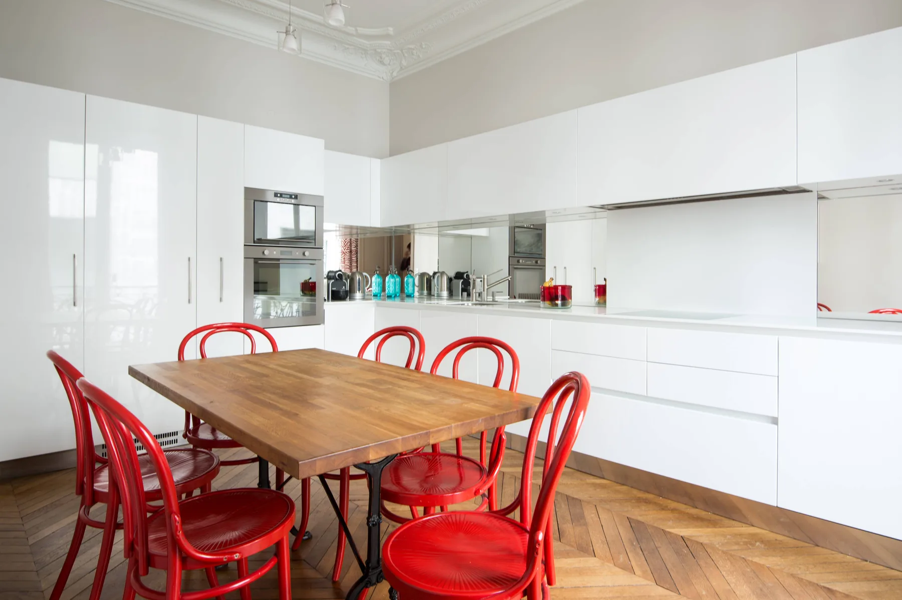 A bright modern kitchen with white cabinets and a wooden dining table.